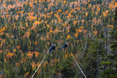 two people sliding down very long and fast zipline during autumn in Stowe, Vermont