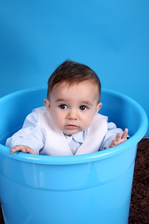 Portrait of a happy baby boy on blue bucket isolated on blue backgroundの写真素材