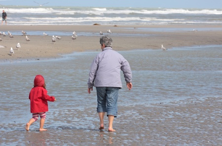 Grandmother and granddaughter walking on the beach with feet in waterのeditorial素材