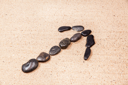 arrow drawn with pebbles on the beach sandの写真素材