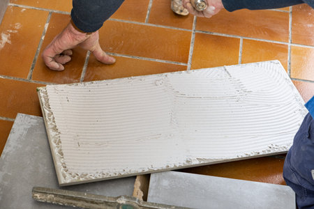 the tiler puts glue on the ceramic tile before laying it