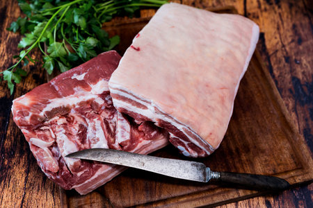fresh pork belly on a used cutting board resting on an old wooden tableの写真素材