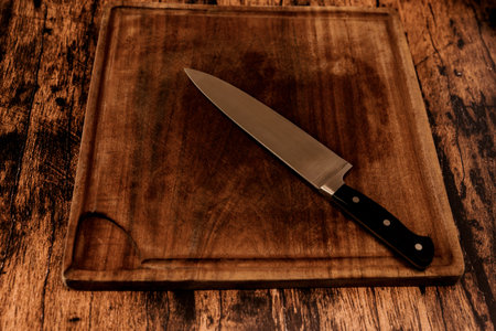 Worn wooden cutting board on an old worn wooden table with an old knife on it