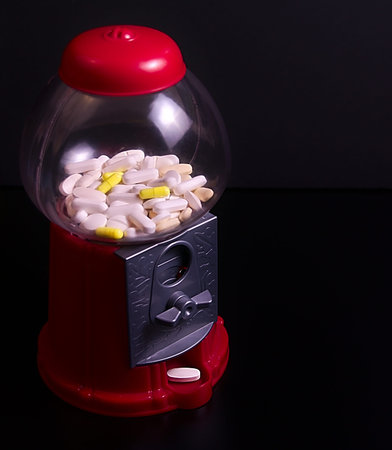 Closeup photo of red plastic sweet machine full of pills, some of them white and some others yellow, and one white pill in the exitの写真素材