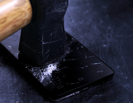 45 degrees close up picture of black mobile phone screen broken by black hammer, all over black boardの写真素材