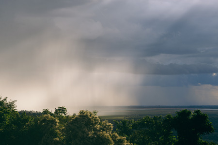 An intense rain storm approaches its rain clouds intercepted by the sunrays of the sunset making for a fantastic view. Registered from a mountain top in the midst of the jungle in Cambodia.のeditorial素材