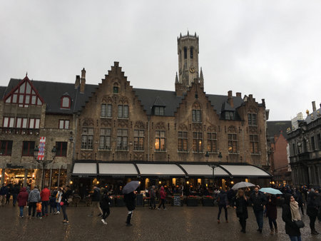 Bruges, Belgium - 8 May 2024: Famous view of Bruges tourist landmark attraction - Rozenhoedkaai canal with Belfry and old houses along canal with tree and tourist boat. Brugge, Belgiumの写真素材