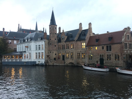 Bruges, Belgium - 8 May 2024: Famous view of Bruges tourist landmark attraction - Rozenhoedkaai canal with Belfry and old houses along canal with tree and tourist boat. Brugge, Belgiumの写真素材