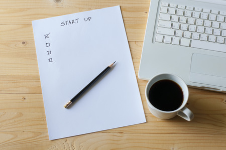 Paper check list for start up business laptop and coffee on wood table.の写真素材