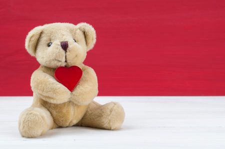 Little bear hold red heart in front red grunge background on white table. Valentines concept.の写真素材