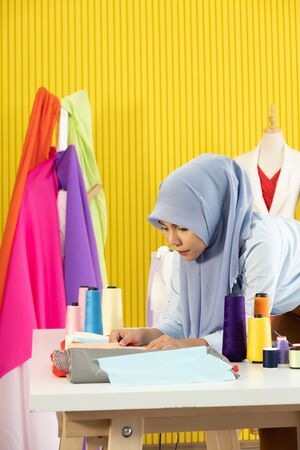 A young beautiful Asian Muslim woman designer who wore a hijab as a startup business owner is considering the fabric to be sewn.の写真素材