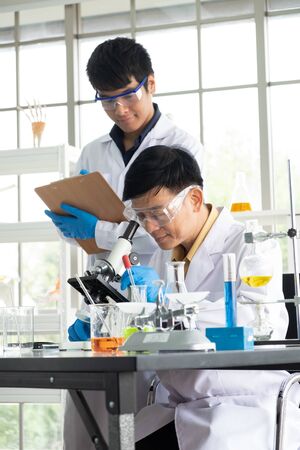Science, Chemistry, Technology, Biology and Laboratory concept - Asian Senior scientist looks into something on a petri dish while Asian junior scientist taking notes.の写真素材