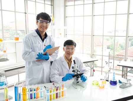 Science, Chemistry, Technology, Biology and Laboratory concept - Portrait of Asian junior scientist is taking notes and Asian Senior scientist works with his microscope.の写真素材