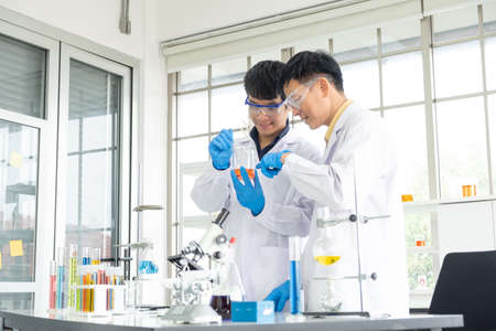 Science, Chemistry, Technology, Biology and Laboratory concept - Asian junior scientist is analyzing experimental results in test glass beaker to Asian Senior scientist.の写真素材