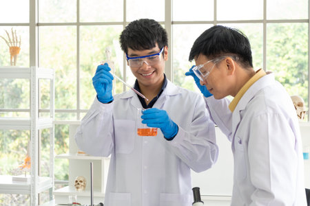 Science, Chemistry, Technology, Biology and Laboratory concept - Asian senior scientist is considering an experiment result in glass beaker of Asian junior scientist.の写真素材