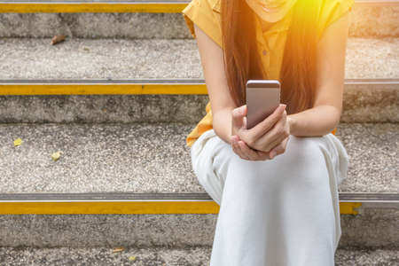 Young woman sitting on stairs with their smartphones, filter colored picture style.の写真素材