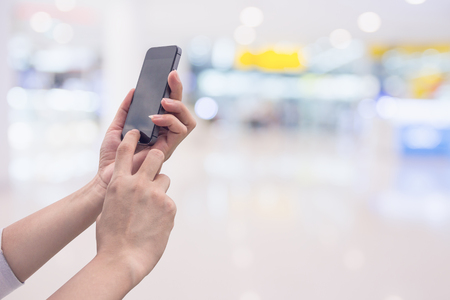 Hand holding smart phone with abstract blur in shopping mall backgroundの写真素材