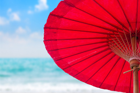 Old fabric red umbrella on blurred beach background.の写真素材