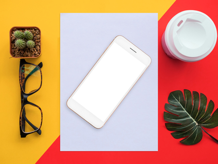 Design flat lay image of workspace desk with smartphone, paper, coffee, cactus, leaf and glasses on red and yellow background.の写真素材