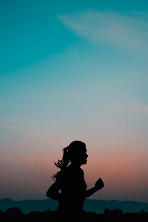 Young woman running at sunrise with mountain natural background.の写真素材