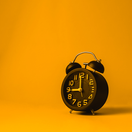 Black vintage alarm clock on yellow background.の写真素材