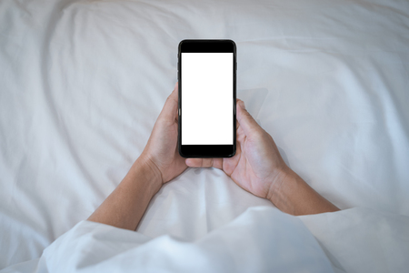 Woman holding on her smartphone while sleeping in bed background.の写真素材