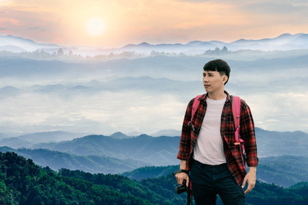 Young hipster photographer holding a camera with beautiful foggy winter sunrise in mountains natural...