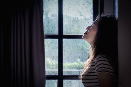 Broken heart young woman is crying in a dark room with rainy season background.の写真素材