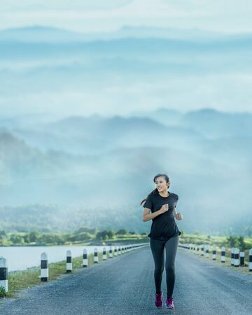 Young woman is running on road in the morning with mountains natural background.の写真素材