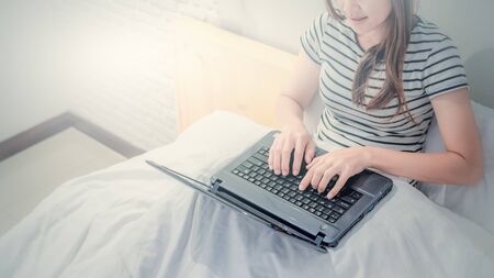 Young Asian woman playing with laptop on her bed in white bedroom background.の写真素材