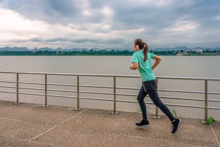 Beautiful woman running on the street with a view of the river in the morning.の写真素材