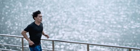 Young man running on the street with a view of the river in the morning.の写真素材