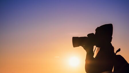 Young hipster woman photographer taking photo with sunset on mountain natural background.の写真素材