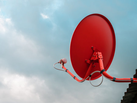Red satellite dish on house roof with sky background.の写真素材