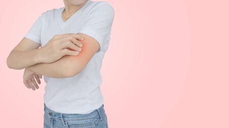 Young woman scratching her elbow on pink wall background.の写真素材