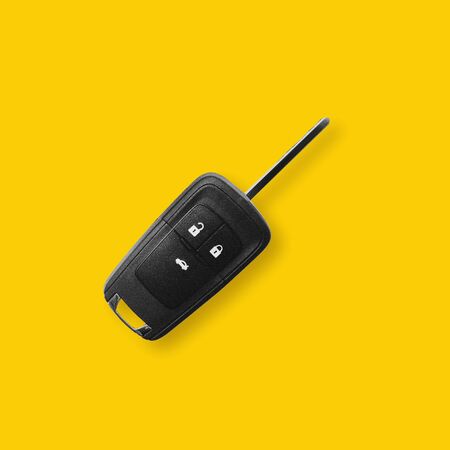 New black car key on yellow background with light shadow.の写真素材