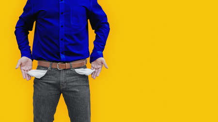 Man wearing a blue shirt showing an empty pockets on yellow wall background.の写真素材