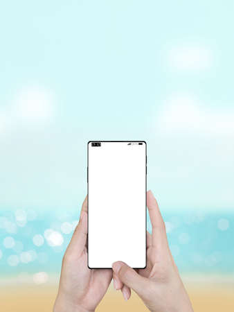 Woman's hand holding smartphone with blur sea natural background.の写真素材
