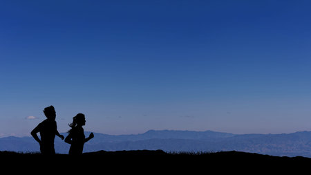 Silhouette image of man and woman trail runner with sky at sunrise while running in the mountains,...