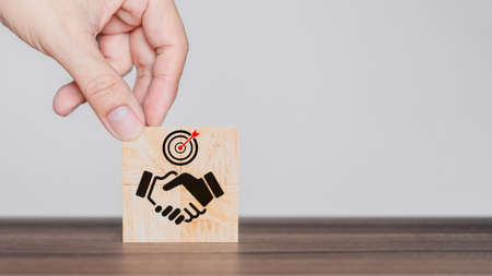 Hand put a handshake icon on wooden cubes block. Business partner or mergers and acquisitions concept. Business common goals and team collaboration.の写真素材