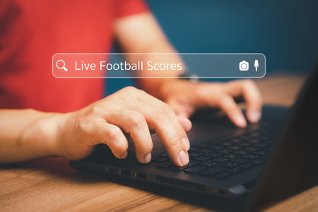 Football fan's hand working with computer laptop on desk in home. Searching Browsing Internet Data...