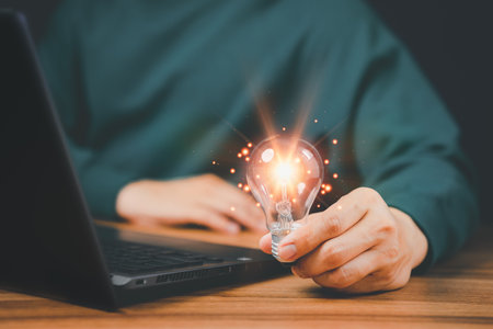 Man holding a light bulb while working on the computer to think and create new ideas with technological innovations and creativity Ideas inspired by online technology, innovations.の写真素材