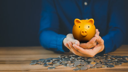 Golden piggy bank on hand with piles of coins for money saving ideas, business finance and investments.の写真素材