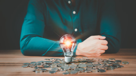 A glowing light bulb on pile money cions on a wooden table, business problem solving ideas and creative marketing ideas Inventing, save money and learning new things.の写真素材