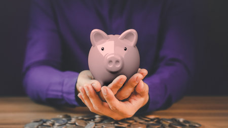 Pink piggy bank on hand with piles of coins for money saving ideas, business finance and investments.の写真素材