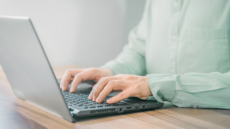 Closeup image of a young man working and typing on laptop computer keyboard on wooden table in the room.の写真素材