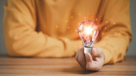 Man holding a glowing abstract light bulb on a wooden table, business problem solving ideas and creative marketing ideas Inventing and learning new things.の写真素材