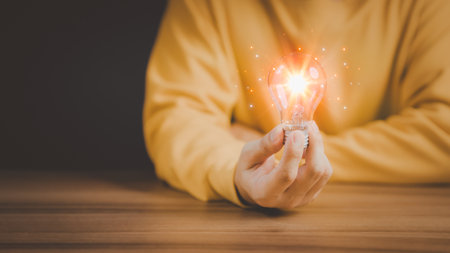 Man holding a glowing abstract light bulb on a wooden table, business problem solving ideas and creative marketing ideas Inventing and learning new things.の写真素材