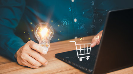 Man holding a light bulb while working on a computer to think and generate new ideas for business profitability with sales and purchases in online stores internet shopping.の写真素材