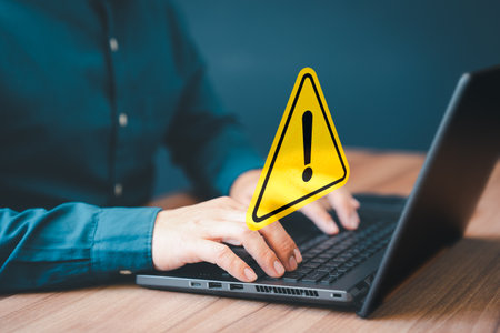 Adult man using computer laptop with triangle caution warning sign for notification error. Computer virus detected, personal data protection, network security and maintenance concept.の写真素材